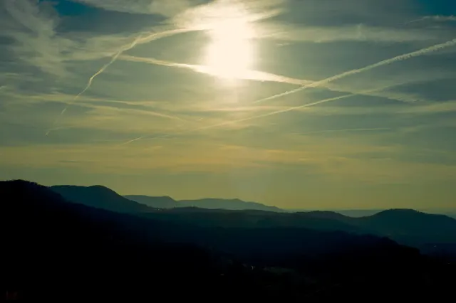 Berglandschaft mit Kondensstreifen und Sonne am Horizont